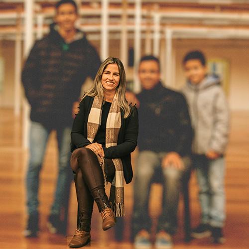 A family made up of a mother, father, and two youths, in an indoor space like a gym or community hall. All except the woman are blurred. When you move the cursor over the image, everyone comes into focus.